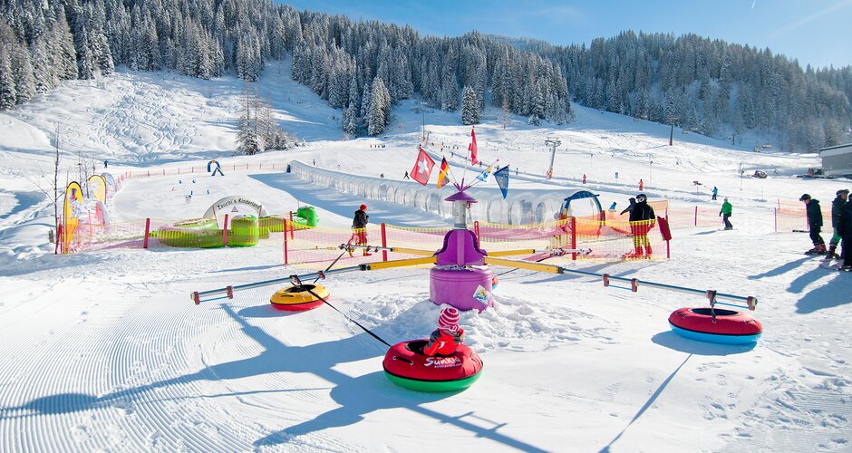 Kinder in Reifenkarussell auf Schneespielplatz mit Förderband und Parcours in Zauchensee