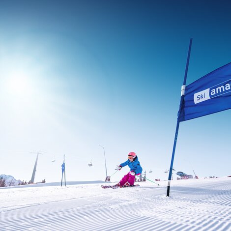 Female skier carves through blue gates on freshly groomed slope under sunshine in Ski amadé