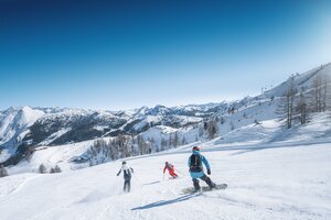 Three winter sports enthusiasts skiing and snowboarding together on the slope
