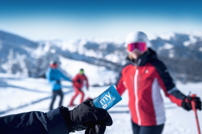 Gloved hand holds blue my Ski amadé Friends Card, with skiers and snowy mountains in background