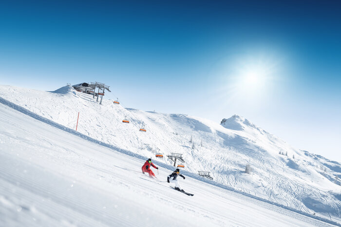 Two skiers carving down a freshly groomed slope on a sunny day | © Ski amadé