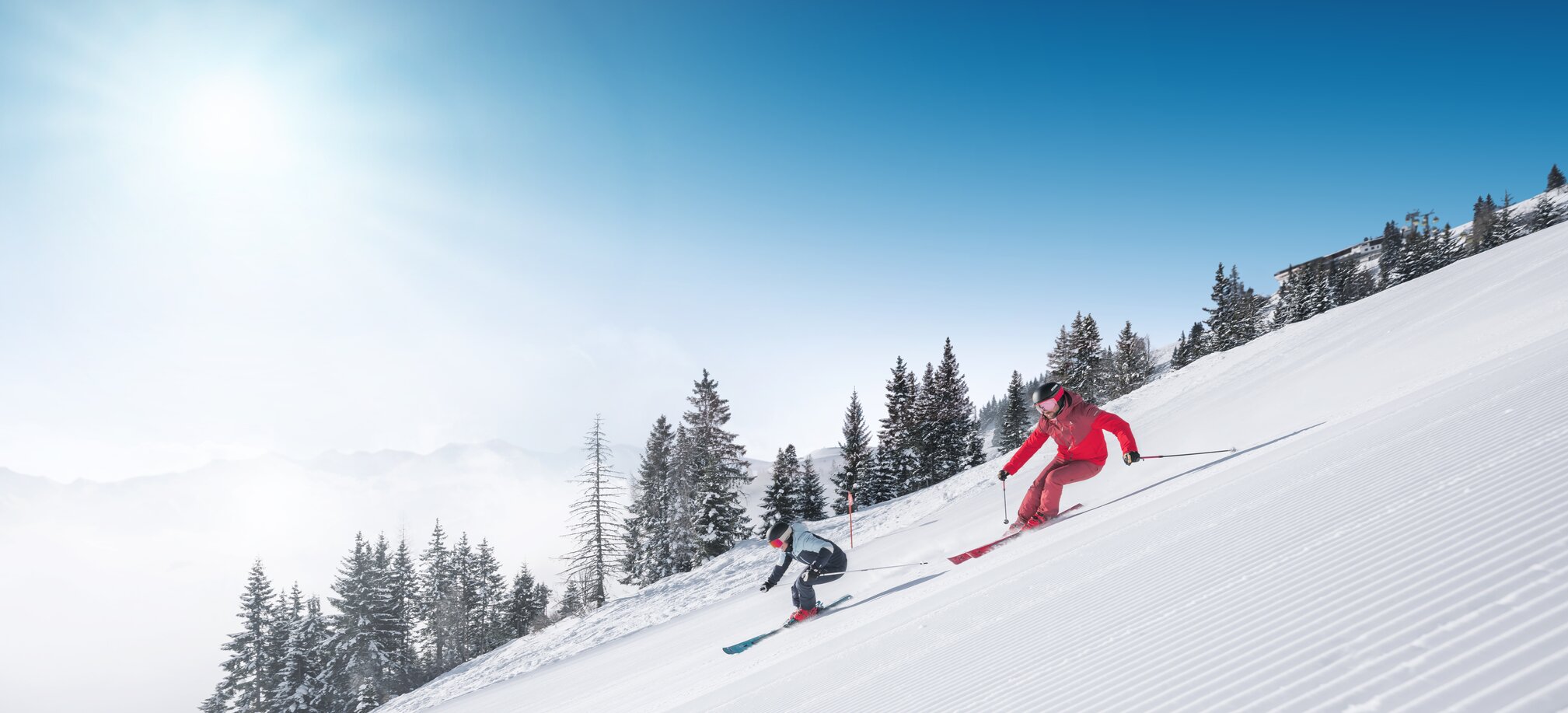 Zwei Skifahrer fahren parallel auf frisch präparierter Skipiste mit Pulverschnee und Sonnenlicht in Ski amadé