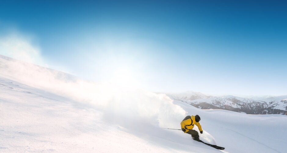 Skier in yellow jacket carves through fresh powder snow on a sunny mountain slope