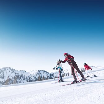 Three skiers skiing down a wide, perfectly groomed slope together.