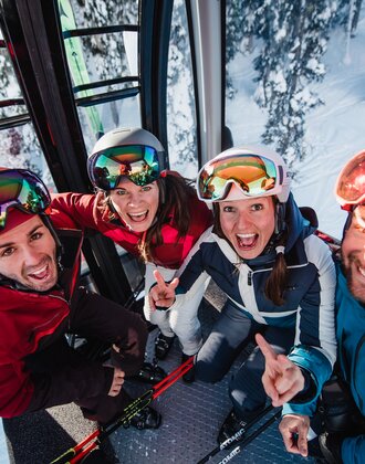 Four skiers laugh and pose happily in a cable car above the ski slope. | © Ski amadé