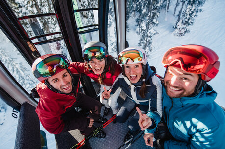 Four skiers laugh and pose happily in a cable car above the ski slope. | © Ski amadé