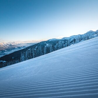 Groomed ski slope with sunrise over snowy mountains. | © Ski amadé