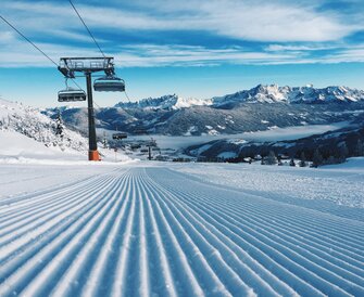 Freshly groomed slope with a chairlift and snow-covered mountains. | © Ski amadé