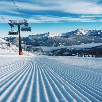 Freshly groomed slope with a chairlift and snow-covered mountains. | © Ski amadé