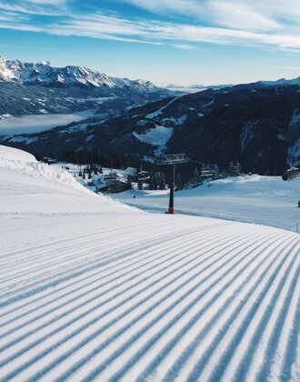 Freshly groomed ski slope with a chairlift and snowy mountains. | © Ski amadé