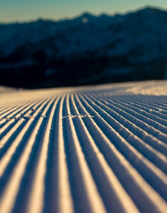 Close-up of a perfectly groomed ski slope at morning light with mountains in the background. | © Ski amadé