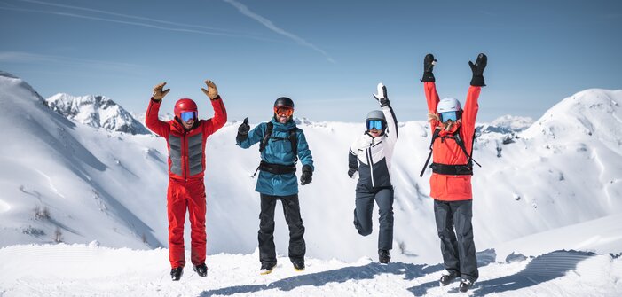 Four skiers jump in the air together with snowy mountain peaks and sunlight in the background