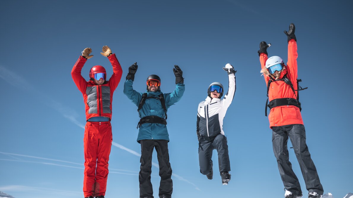Vier Skifahrer springen gleichzeitig in die Luft vor blauem Himmel und verschneiten Bergen | © Ski amadé