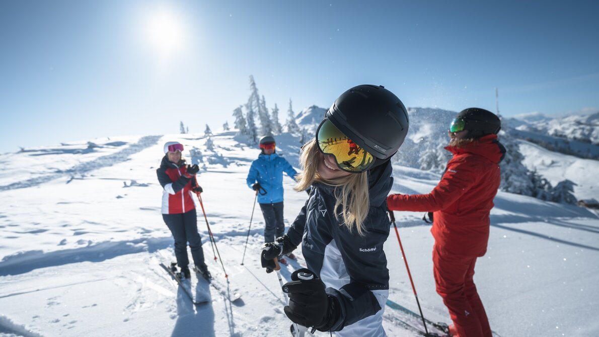 Vier Skifahrer genießen die Sonne auf einer verschneiten Piste. Eine Frau im Vordergrund lacht in die Kamera. | © Ski amadé