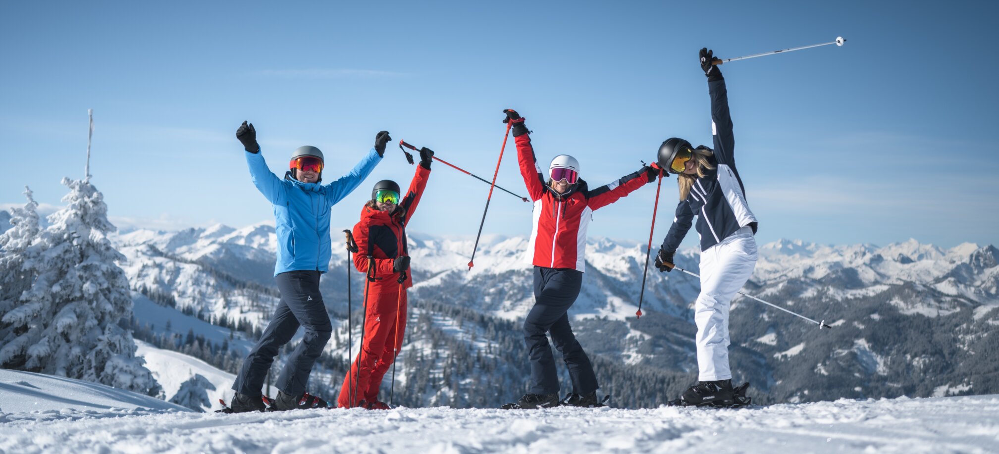 Vier Freunde in Skiausrüstung stehen auf der Piste und Strecken die Arme freudvoll in die Höhe. | © Ski amadé