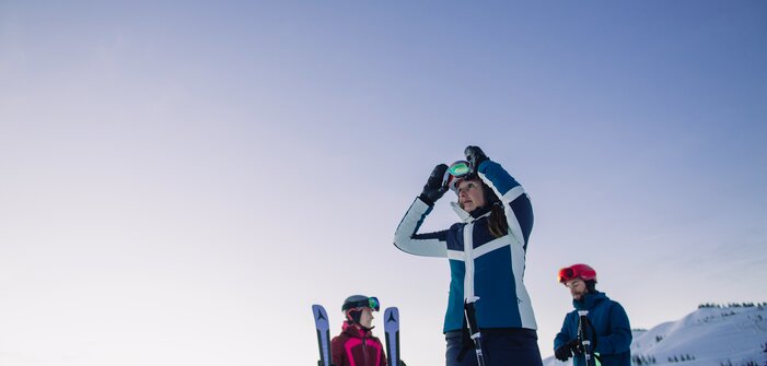 Drei Skifahrer stehen im Schnee, eine Frau setzt ihre Skibrille auf. | © Ski amadé
