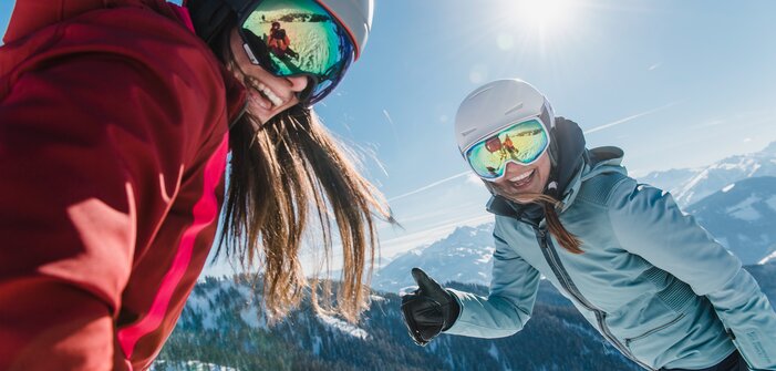 Two female skiers laugh at the camera, one giving a thumbs-up. | © Ski amadé