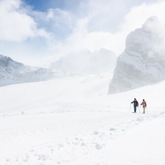 Two ski tourers walk side by side through snowy mountain landscape with rocky peaks | © Harald Steiner