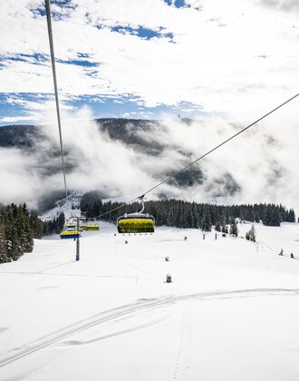 Yellow chairlift over snowy slopes and forest in misty winter mountain scenery | © filzmoos.ski