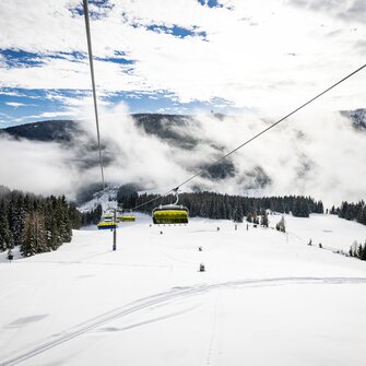 Yellow chairlift over snowy slopes and forest in misty winter mountain scenery | © filzmoos.ski
