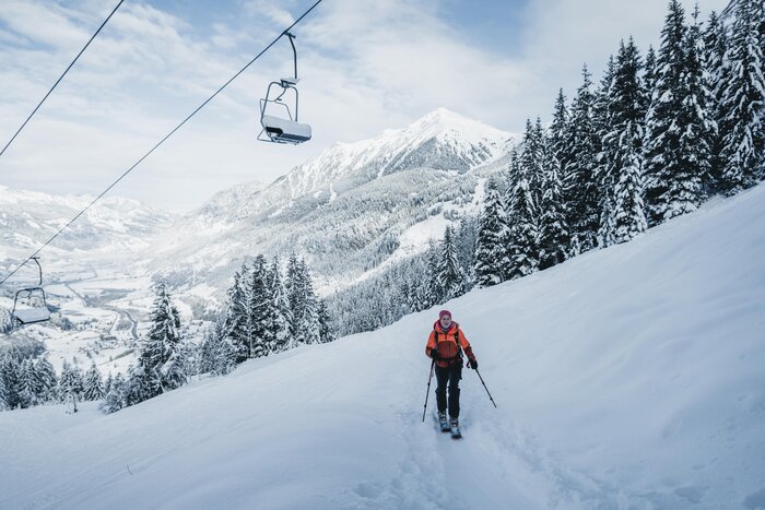 Female ski tourer climbs Graukogel under lift with scenic valley view and snow-covered trees | © Gasteinertal Tourismus GmbH, Christoph Oberschneider