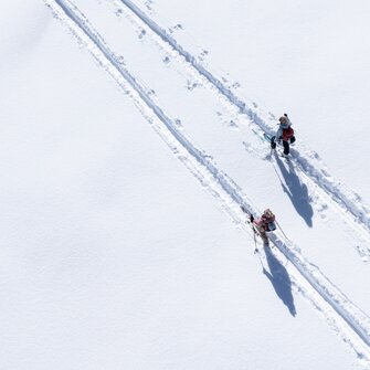 Zwei Pistentourengeher mit Stöcken auf verschneiter Spur bei Sonne auf der Planai unterwegs | © Josh Absenger