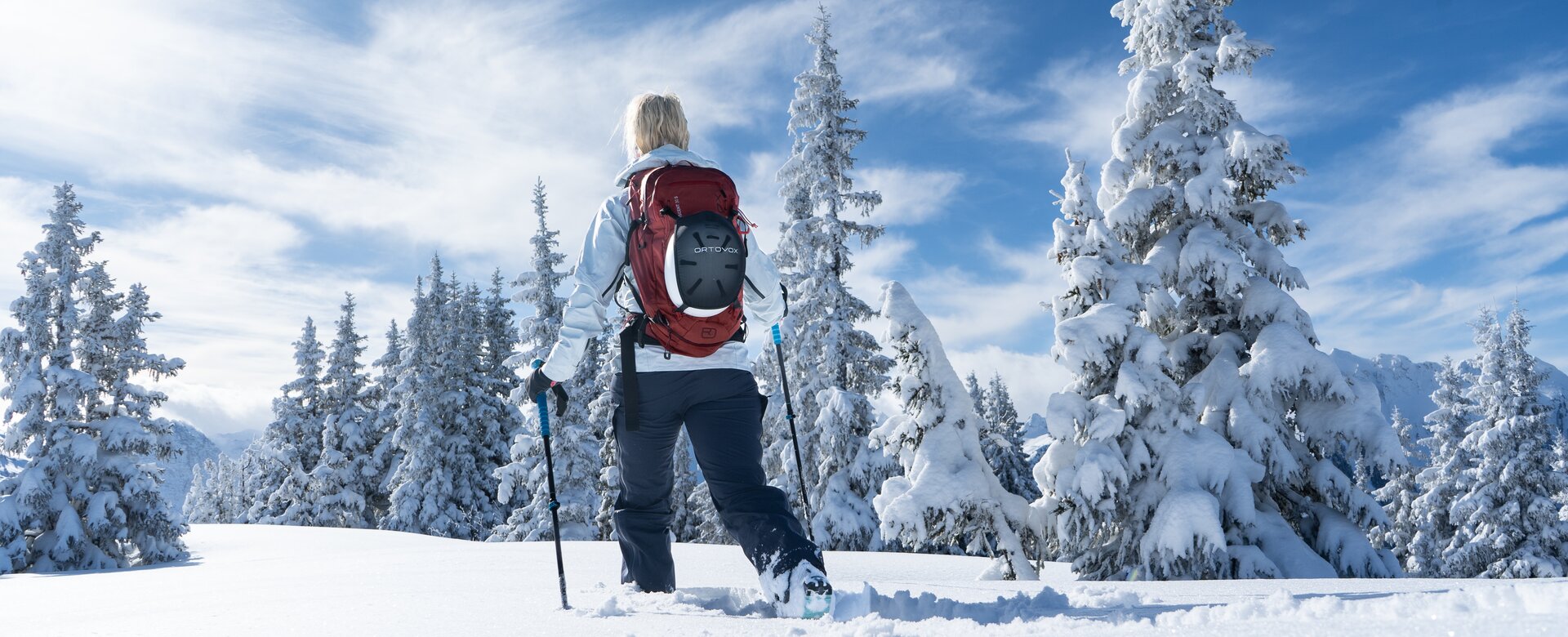 Frau mit rotem Rucksack wandert mit Schneeschuhen durch tief verschneiten Winterwald | © Josh Absenger