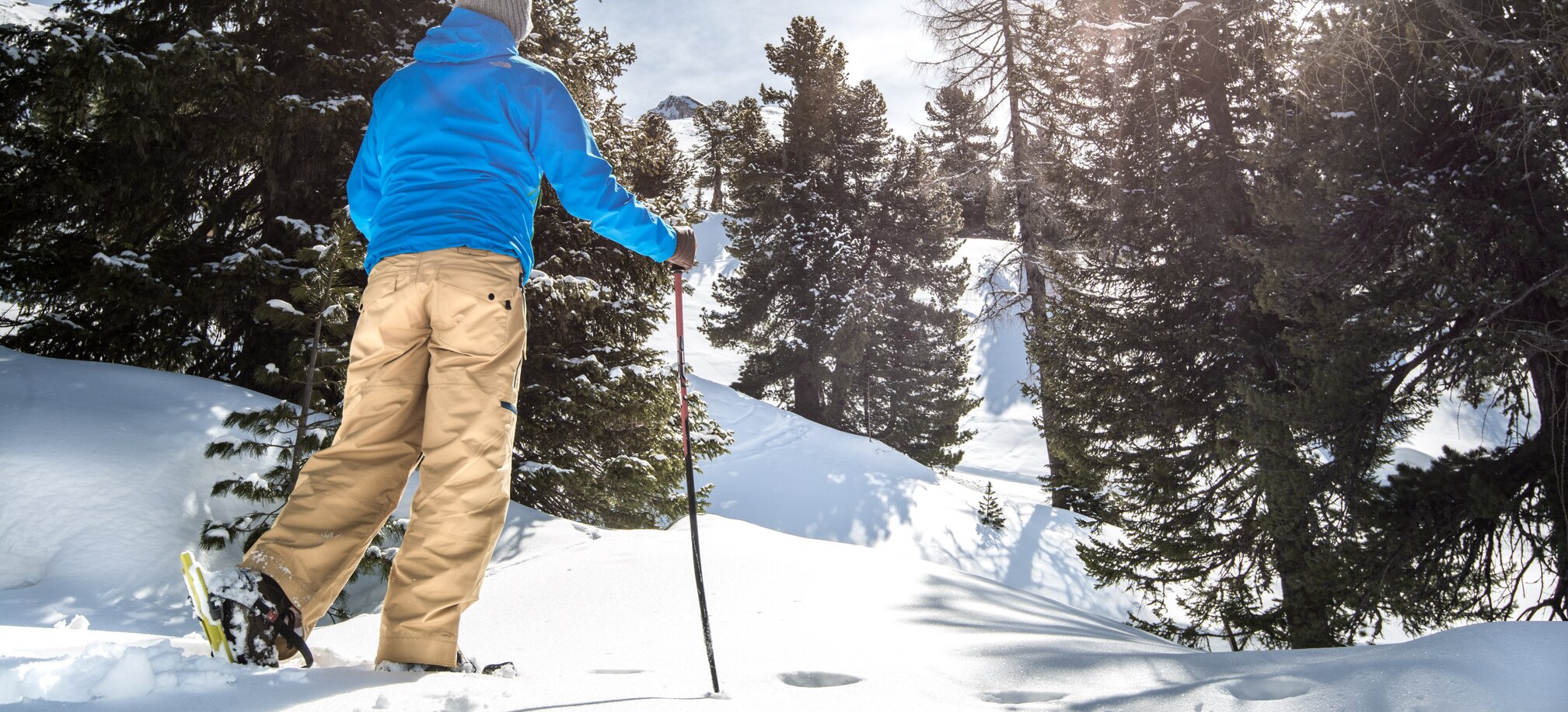Person mit Schneeschuhen und Wanderstock im verschneiten Waldgebiet bei Sonne in Gastein | © Gasteinertal Tourismus GmbH
