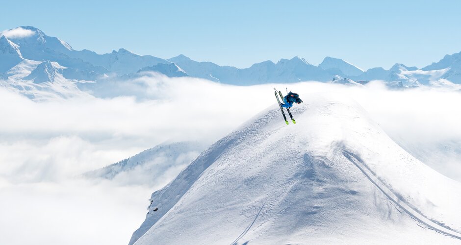 Skier doing a backflip over a snow dome and all around are snowy mountains and a blue sky | © Gasteinertal Tourismus GmbH, www.oberschneider