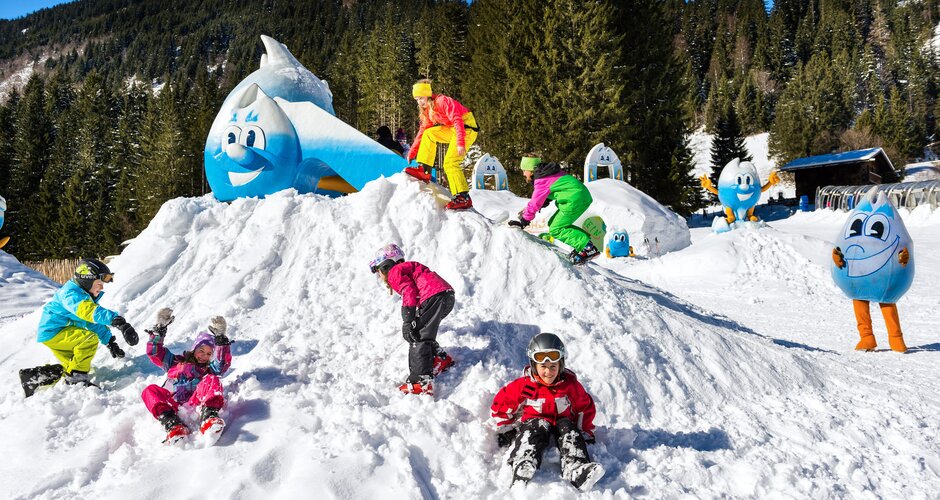 Kinder beim Spielen auf einem Schneehügel mit Maskottchen Gasti im Kinderpark Gastein | © Gasteiner-Bergbahnen AG