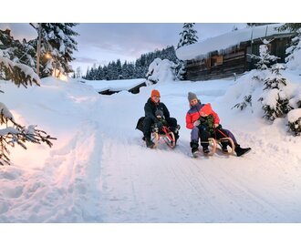 Eltern mit Kindern beim gemeinsamen Rodeln im Winterurlaub in Gastein | © GTG