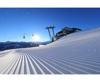 The rising sun illuminates the freshly prepared piste and the cable car passes over it | © Tourismusverband Großarltal