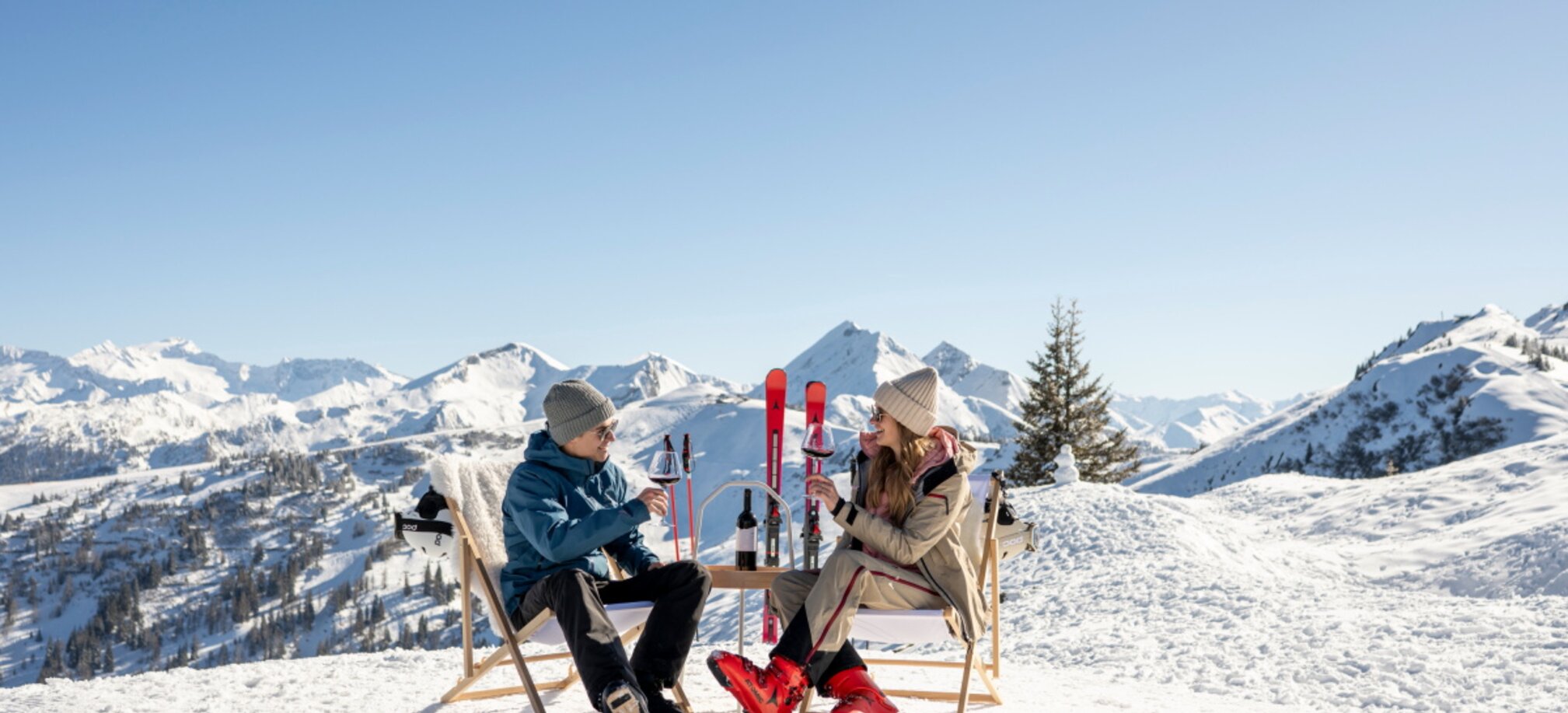 Two skiers sit on deck chairs in the snow in Grossarltal drinking wine with view of snowy mountains | © Lorenz Masser
