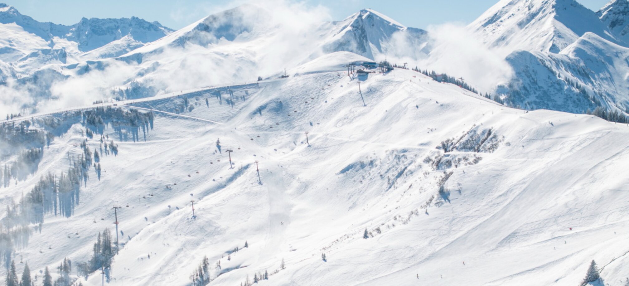 Wide view of the Grossarltal ski area with groomed slopes, lifts, snowy peaks and drifting mountain clouds | © Lorenz Masser