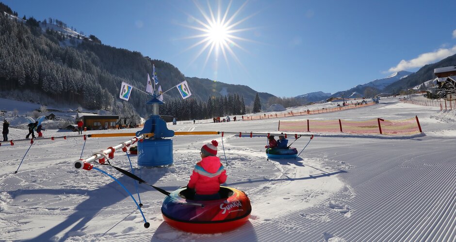 Kinder fahren mit Reifenkarussell auf der verschneiten Erlebniswiese im Großarltal bei Sonnenschein