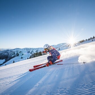 Ein Skifahrer in sportlicher Haltung auf frisch präparierter Piste bei Sonnenschein