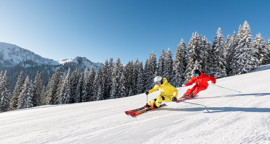 Zwei Skifahrer in gelber und roter Kleidung fahren parallel auf verschneiter Piste | © Hochkönig Tourimus GmbH