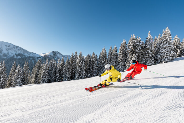 Zwei Skifahrer in gelber und roter Kleidung fahren parallel auf verschneiter Piste | © Hochkönig Tourimus GmbH