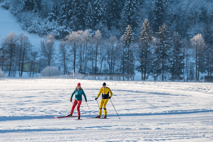 Zwei Langläufer auf präparierter Loipe in winterlicher Landschaft mit verschneiten Bäumen im Hintergrund | © Salzburger_Sportwelt_Lorenz_Masser