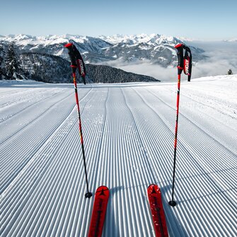 Two ski poles are stuck in the freshly groomed piste and the ski tip can also be seen as well as a snow-covered mountain landscape in the distance | © Snow Space Salzburg Christian Schartner