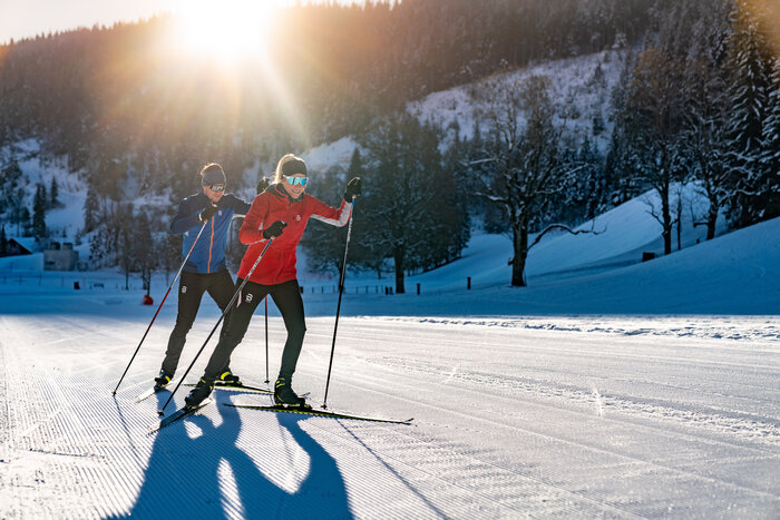 Zwei Langläufer in Sportkleidung laufen bei tiefstehender Sonne auf gespurter Loipe in Ramsau am Dachstein | © Christine Höflehner