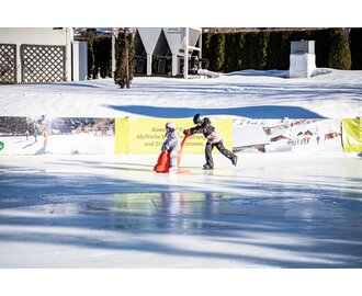 Zwei Kinder mit Helm und bunter Kleidung beim Eislaufen mit Lernhilfe auf Eisbahn im Winter | © Gerhard Pilz