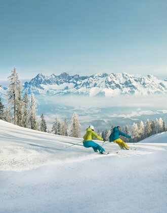 Zwei Skifahrer auf präparierter Piste, verschneite Bäume und Bergkulisse im Hintergrund | © © Peter Burgstaller – Schladming-Dachstein