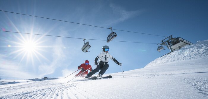 Two skiers carving beneath lift in bright mountain sun