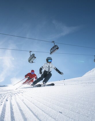 Two skiers carving beneath lift in bright mountain sun