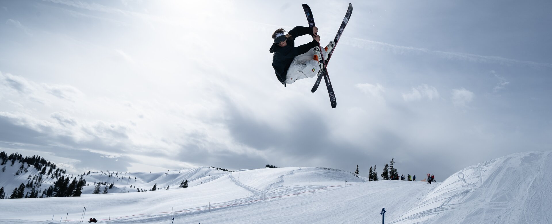 Ein Freestyler springt über eine Schanze im Kings Park und macht einen Trick mit überkreuzten Skiern.