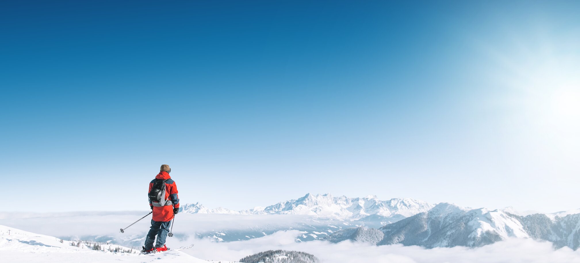 Skier with red ski jacket stands on the snow and looks at the surrounding mountains