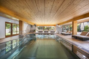 Hallenbad im Tirolerhof mit Holzdecke, Steinwand, Liegen und Panoramafenstern