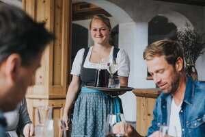 Kellnerin im Dirndl serviert Rotwein und Weißwein im Hotelrestaurant