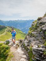 Wanderer auf schmalem Bergpfad zwischen Felsen mit weitem Blick über grüne Gasteiner Alpenlandschaft | © Gasteinertal Tourismus GmbH, Oberschneider